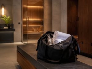 Premium gym locker room bench with workout bag and towels leading to a glowing cedar sauna glass door.